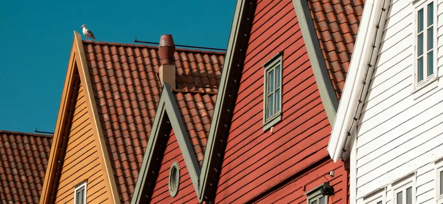 Fachadas rojas y amarillas de las casas de madera de Bryggen, Bergen, Noruega, con tejas y gaviota en el tejado.