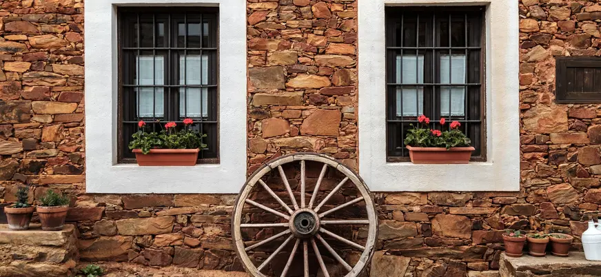 Fachada de casa maragata de piedra en Castrillo de los Polvazares, León, con una rueda de carro y dos ventanas.