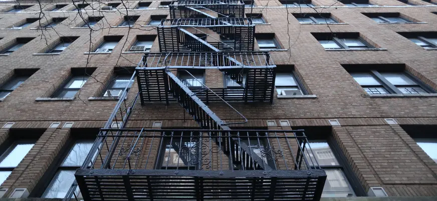 Contrapicado de un edificio de ladrillo en Nueva York con una escalera de incendios metálica y negra en la fachada.
