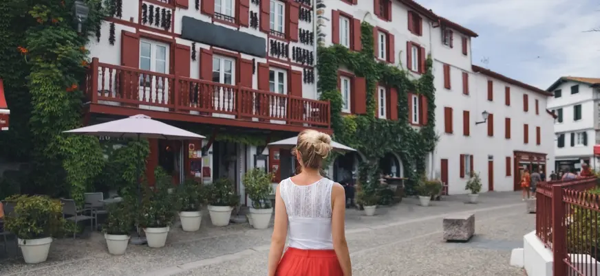 Mujer paseando entre casas con contraventanas rojas en Espelette, pueblo del País Vasco francés.