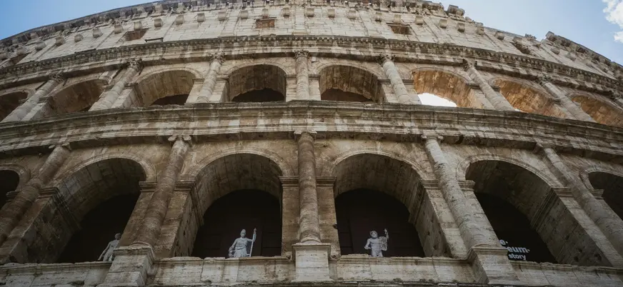 Fachada del Coliseo de Roma vista desde abajo con arcos y estatuas en las galerías