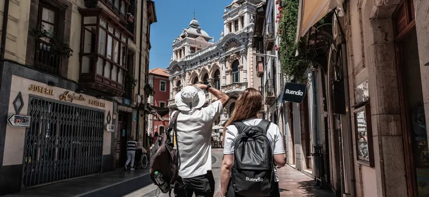 Turistas paseando por una calle del centro histórico de Llanes, admirando la arquitectura típica asturiana bajo el sol.