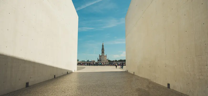 Vista del Santuario de Fátima, Portugal, enmarcada por muros de hormigón, con la torre de la Basílica de fondo.