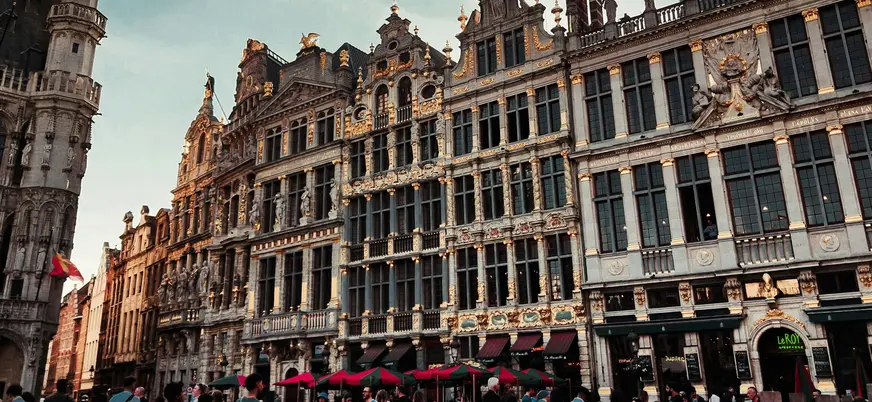 Personas disfrutando en terrazas al aire libre frente a los históricos y ornamentados edificios de la Grand Place de Bruselas.