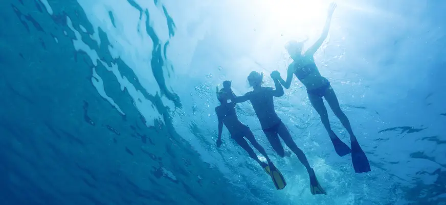 Siluetas de tres personas buceando bajo el mar en Menorca