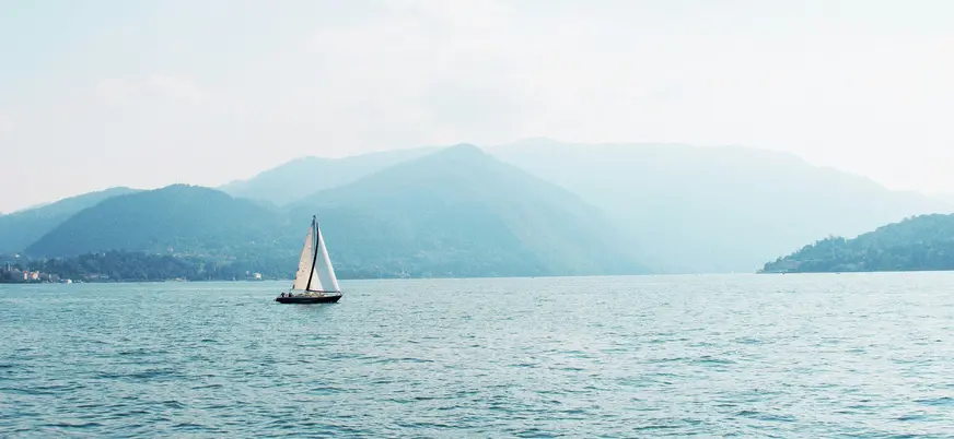 Velero navegando en el Lago di Como con montañas en el horizonte