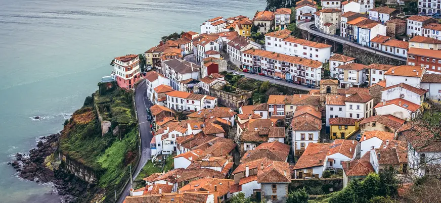 Panorámica de Lastres, Asturias, pueblo marinero de casas con tejados naranjas en un acantilado costero.