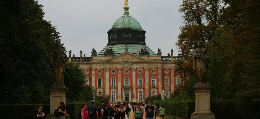 Entrada del Nuevo Palacio (Neues Palais) en Potsdam, Alemania. Edificio barroco con cúpula verde, estatuas y personas.
