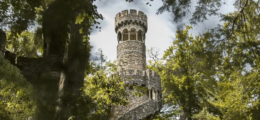 Torre de piedra con escalera en espiral entre árboles en los jardines de la Quinta da Regaleira.