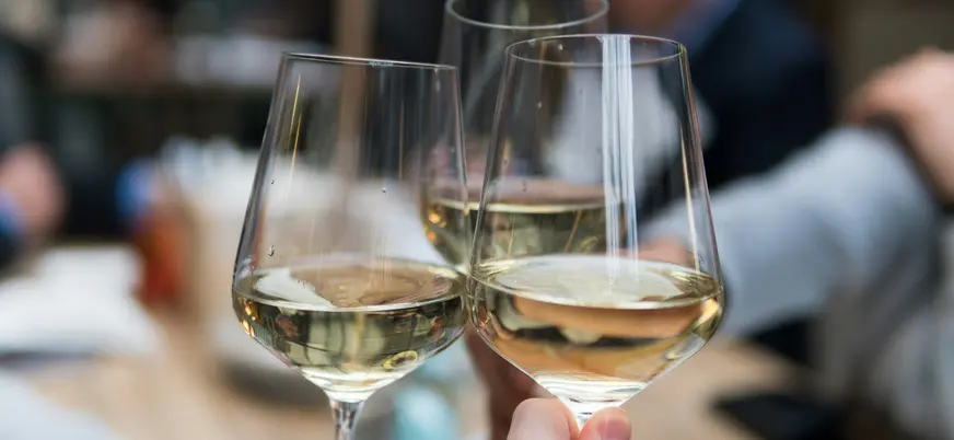 Brindis con copas de vino blanco, enfoque cercano en las manos y el cristal.