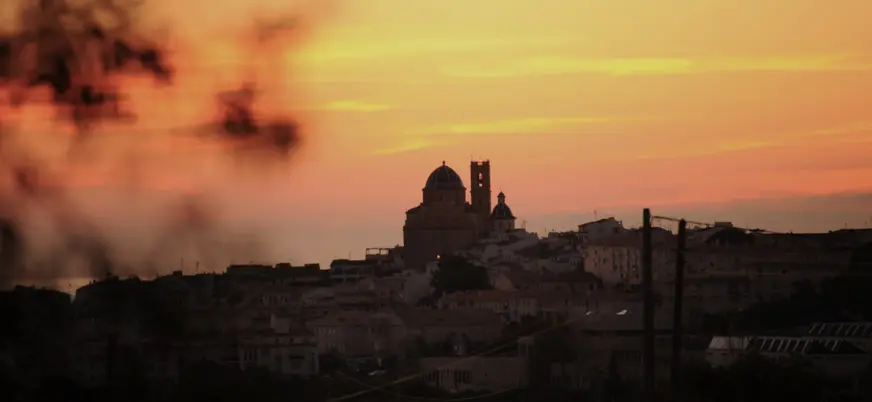Silueta de la iglesia de Altea, con sus cúpulas azules, recortada contra un cielo de amanecer en tonos naranja y rojo.