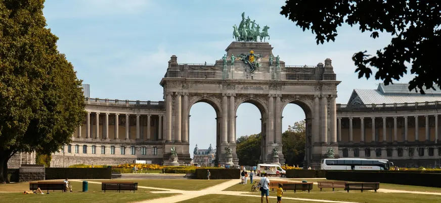 Arco del Triunfo en el Parque del Cincuentenario de Bruselas, con personas paseando y áreas verdes al frente.