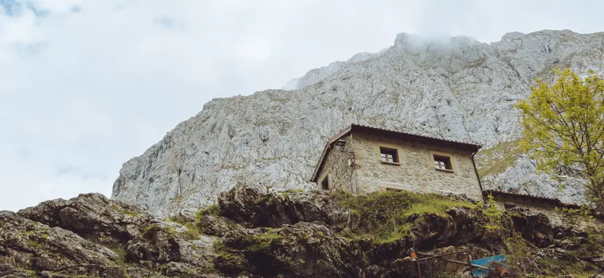 Casa de piedra en el pueblo de Bulnes, construida sobre la ladera rocosa de los Picos de Europa y rodeada de naturaleza.