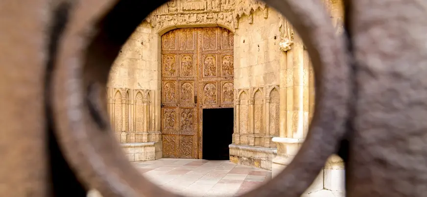 Puerta de madera tallada de la Catedral de León, estilo gótico, vista a través de una reja o mirilla de hierro forjado.