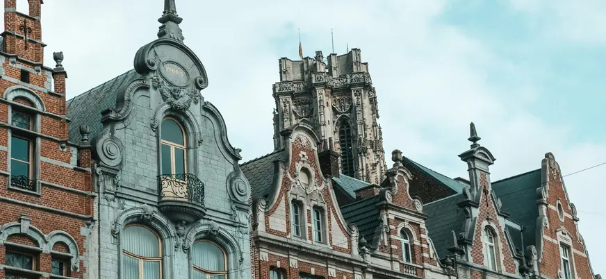 Casas gremiales históricas de piedra y ladrillo en Malinas (Mechelen), Bélgica, con la Torre de San Rumoldo detrás.
