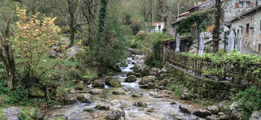 Río en Bulnes, Asturias, rodeado de casas de piedra, vegetación verde y un entorno natural de montaña.