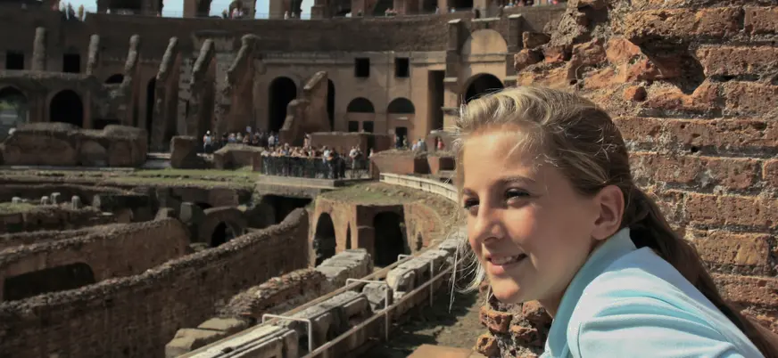 Niña observando el interior del Coliseo de Roma desde un mirador entre ruinas