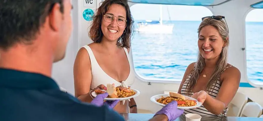 Turistas recibiendo paella en un paseo por las calas del sur de Ciudadela