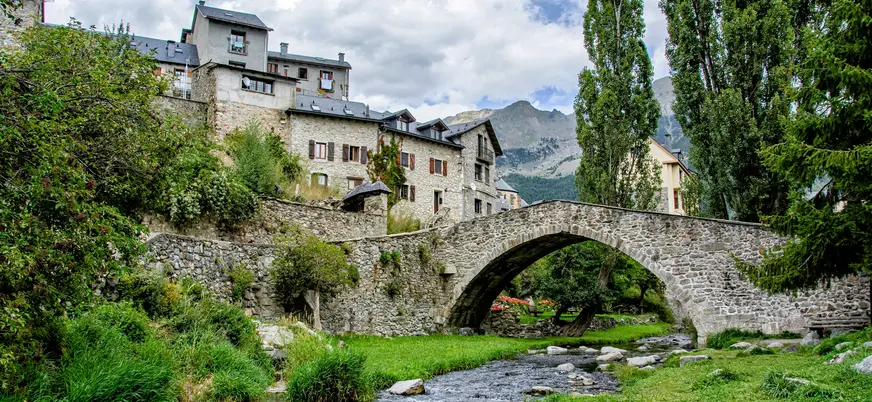 Puente de piedra sobre el río en Sallent de Gállego, con casas tradicionales pirenaicas y montaña de fondo, Huesca.