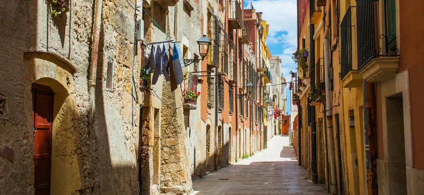 Callejuela estrecha soleada en el casco antiguo de Tarragona, con edificios de piedra y colores cálidos