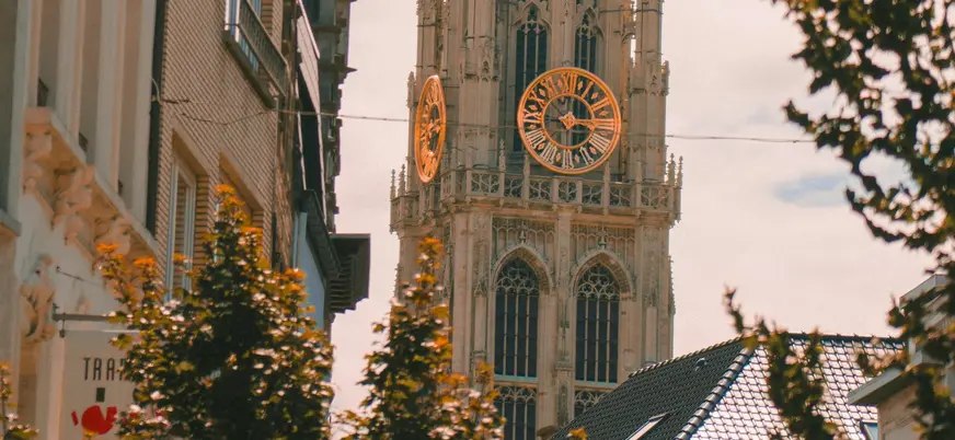 Torre de la Catedral de Nuestra Señora de Amberes, Bélgica, con sus grandes relojes dorados, vista entre edificios.