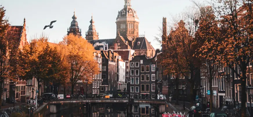 Canal de Ámsterdam con edificios reflejados en el agua y árboles otoñales