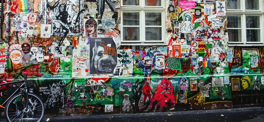 Pared repleta de arte urbano, pegatinas y grafitis coloridos en un callejón alternativo de Berlín