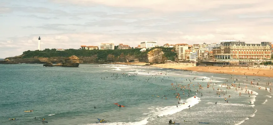 Playa de Biarritz con surfistas en el agua y edificios junto a la costa.