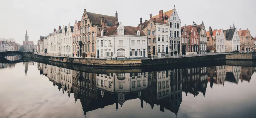 Casas históricas reflejadas en el canal principal de Brujas en un día nublado