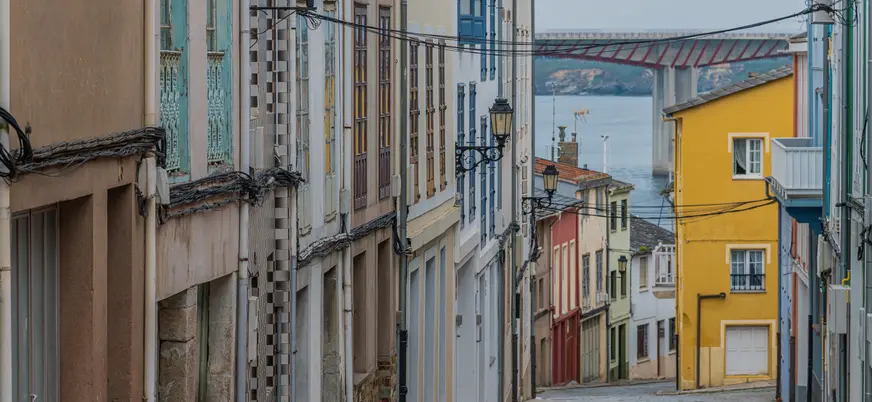 Calle del casco antiguo de Ribadeo con fachadas coloridas, vistas al mar Cantábrico y al puente de los Santos al fondo.