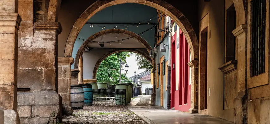 Arcos de piedra en una calle del casco antiguo de Avilés, con mesas y barriles típicos bajo los soportales asturianos.