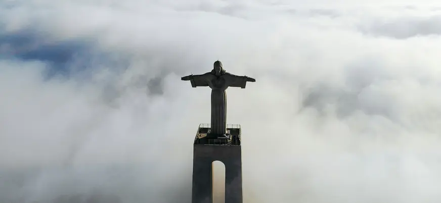 Cristo Rei emergiendo entre nubes sobre Lisboa en una vista aérea