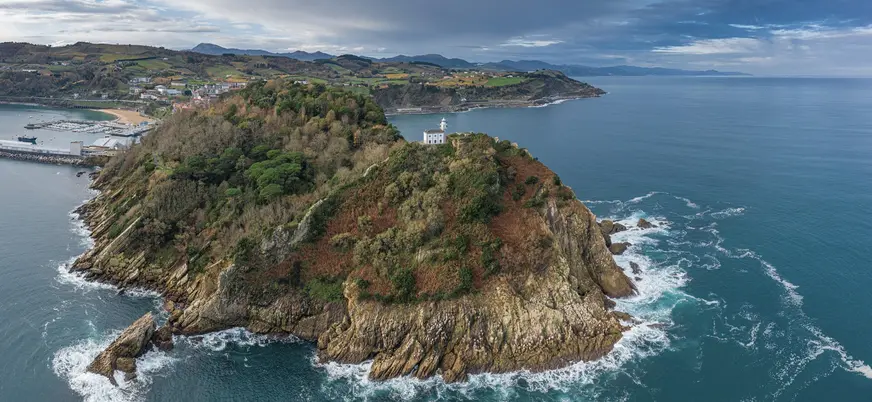 Isla con faro en la costa de Getaria rodeada por acantilados y mar.