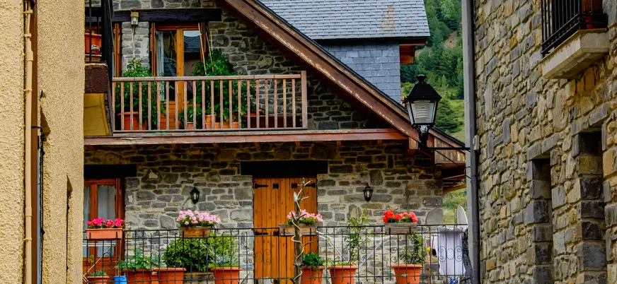 Fachada de casa de piedra tradicional en Jaca, Pirineo Aragonés, con balcones de madera decorados con macetas y flores.