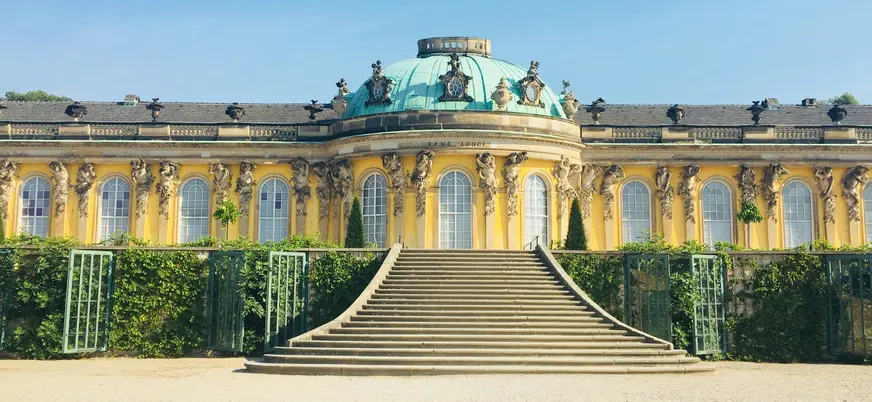 Gran escalinata que sube al Palacio de Sanssouci en Potsdam, Alemania, destacando su fachada amarilla y cúpula verde.