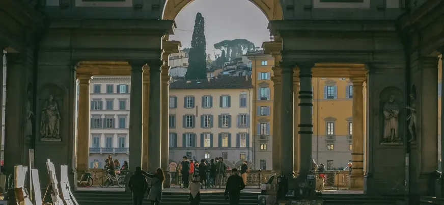 Vista desde el patio de la Galería Uffizi en Florencia, Italia, mostrando arcos monumentales, esculturas clásicas y edificios históricos iluminados por la luz del atardecer.