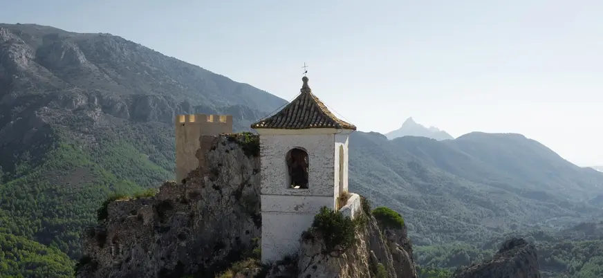 Campanario de Guadalest sobre un peñasco, rodeado de montañas y paisaje natural.