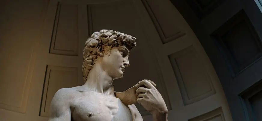 Escultura del David de Miguel Ángel en la Galería de la Academia de Florencia, mostrando detalles del torso y la mano que sostiene la piedra, con fondo arquitectónico clásico.