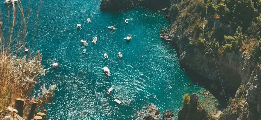 Vista de una  pequeña cala desde los acantilados, con embarcaciones de recreo en el mar.