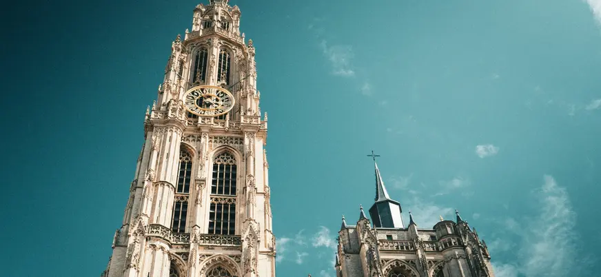 Torre gótica y fachada de la Catedral de Nuestra Señora de Amberes, Bélgica, con cielo azul turquesa dramático.