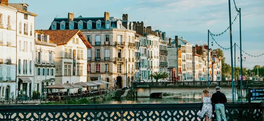 Río y casas al atardecer en Bayona, con parejas apoyadas en el puente.