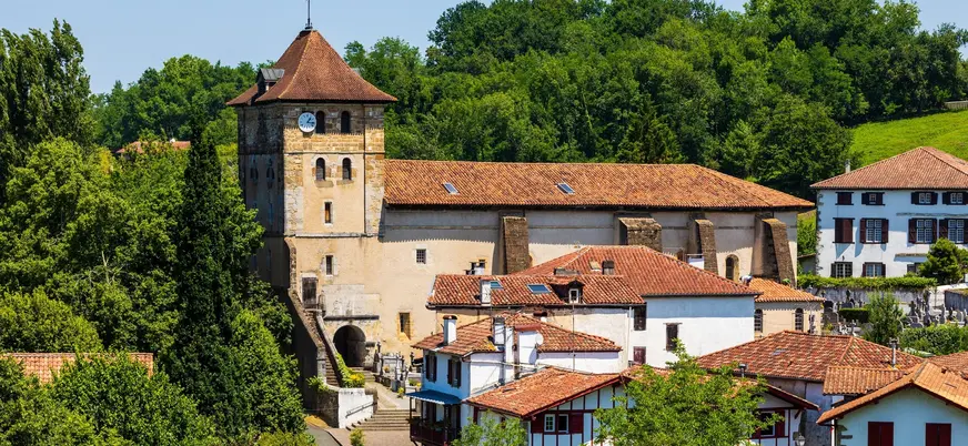 Iglesia de San Esteban rodeada de casas tradicionales blancas y bosque en el pueblo navarro de Bera.