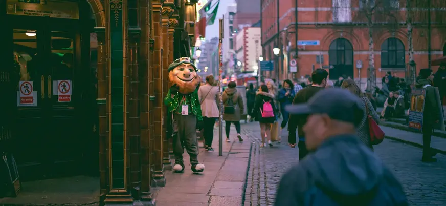 Personaje disfrazado de duende irlandés parado en la entrada de un pub.