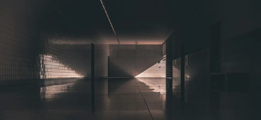 Pasillo interior oscuro en Fátima con suelo reflectante y un rayo de luz que irradia desde el fondo.