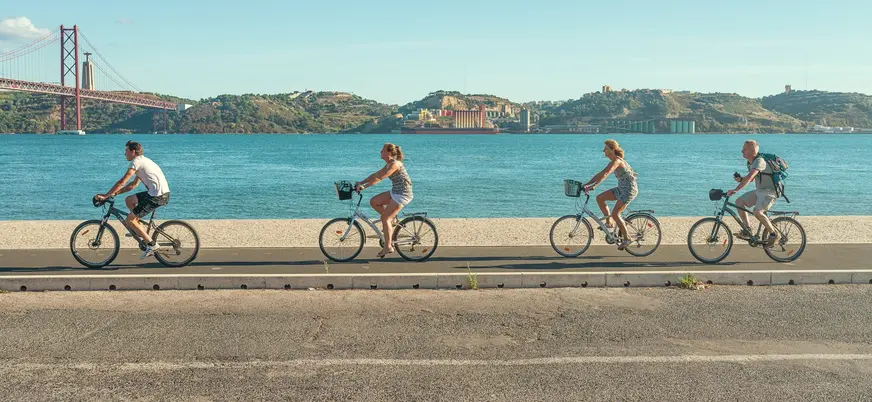 Grupo en bicicleta junto al río Tajo con vistas al Puente 25 de Abril en Lisboa