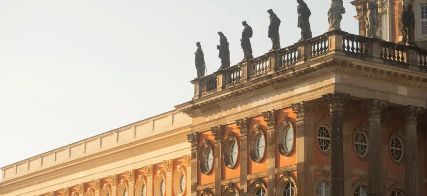  Detalle de la fachada del Nuevo Palacio (Neues Palais) en Potsdam, con ladrillo rojo, columnas y estatuas en el tejado.