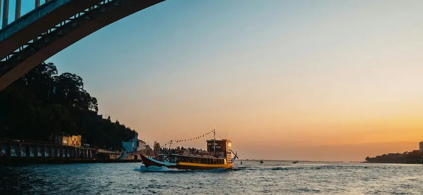 Barco turístico navegando al atardecer junto al puente de Arrábida en Oporto.
