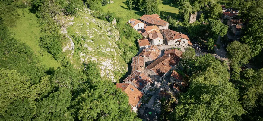 Vista aérea del pueblo de Bulnes, Asturias, en Picos de Europa, rodeado de vegetación verde y montañas.