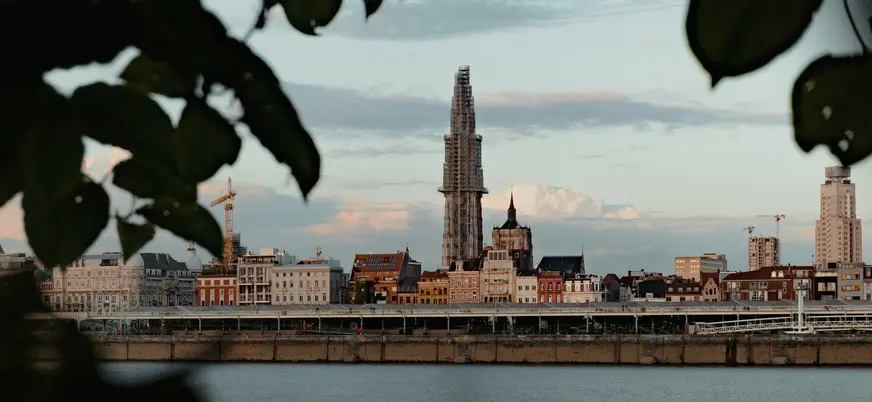 Horizonte de Amberes, Bélgica, con la torre de la Catedral en restauración, vista desde el río Escalda, a través de hojas.