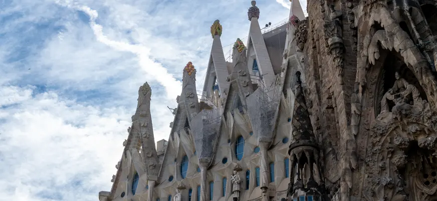Detalle lateral de la Sagrada Familia con sus torres y esculturas bajo el cielo azul